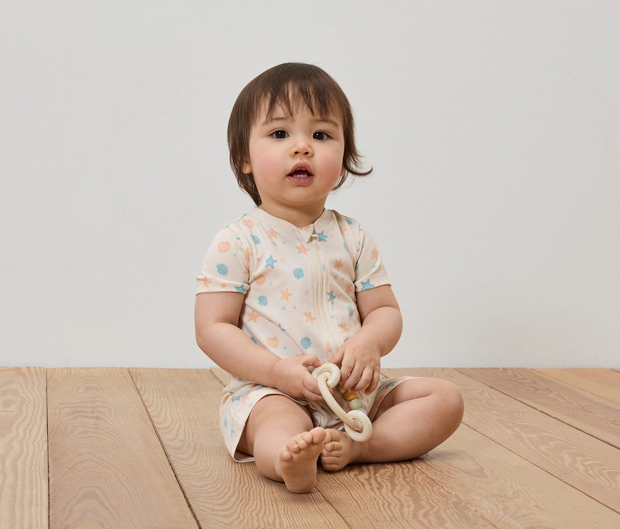 Ein Baby sitzt auf einem Holzboden und hält ein Spielzeug.