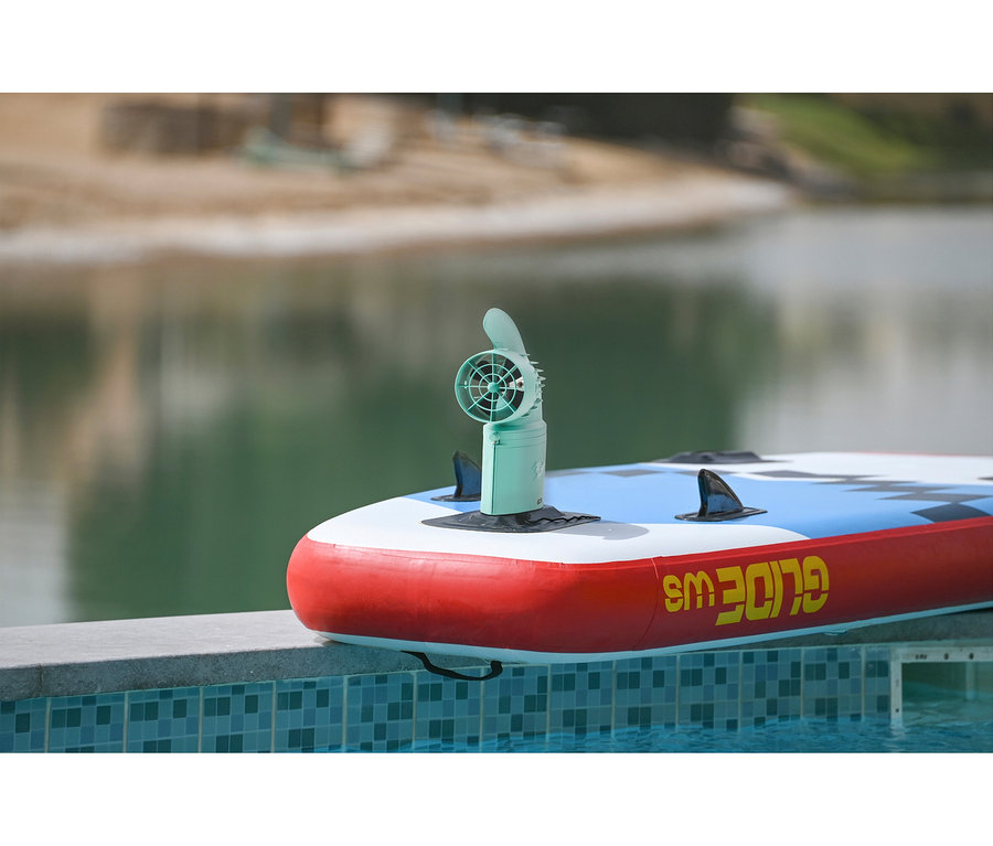 Ein rot-weiß-blaues Stand-Up-Paddle-Board mit einem grünen Elektromotor liegt am Pool.