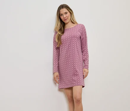 Frau mit langen blonden Haaren, die ein rosafarbenes, langärmeliges Kleid mit geometrischem Muster vor einer weißen Wand trägt.