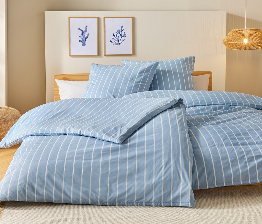 Bett mit blau-weiß gestreifter Bettwäsche, zwei Kissen und zwei Bilder an der Wand.