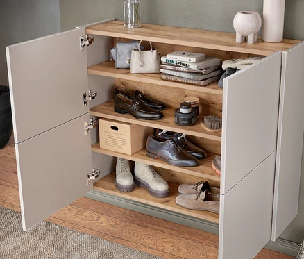 Offener Holzschuhschrank mit grauen Schuhen, Handtaschen und Pflegeprodukten.