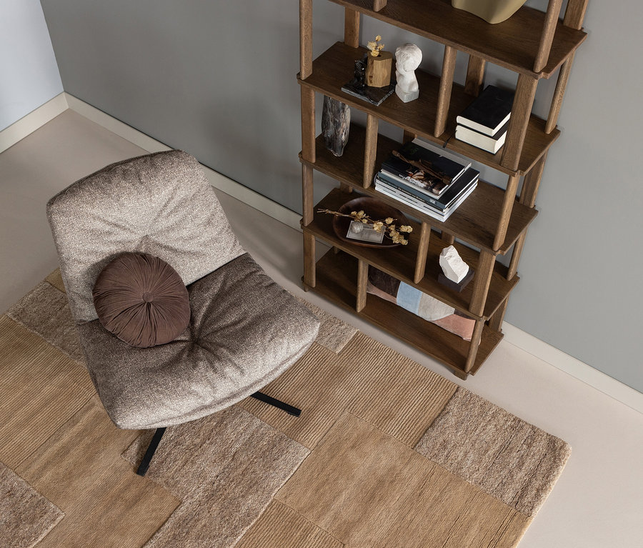 Sessel mit braunem Kissen auf sandfarbenem WOOOD Handwebteppich »Noven«, 170 x 240 cm. Holzregal im Hintergrund.