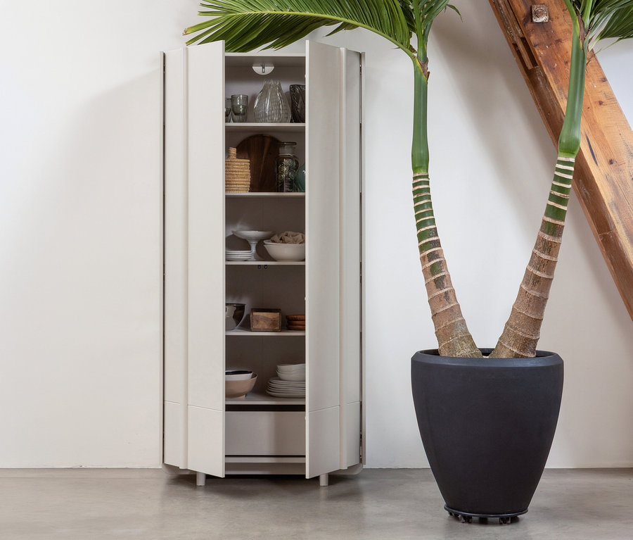 Offener, staubfarbener WOOOD Lagerschrank »Basu« Kiefer mit Geschirr und Deko neben einer Topfpflanze vor einer Wand.