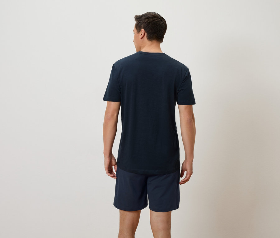 Mann von hinten in marineblauem T-Shirt und Shorts vor einem neutralen Hintergrund.