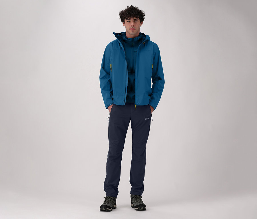 Mann in blauer Jacke und CMP Herren-Stretch-Nylon-Wanderhose. Er steht vor einem hellen Hintergrund.