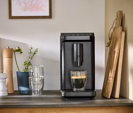 Auf einer Küchentheke steht eine schwarze »Esperto mini« und bereitet Kaffee in einem Glas zu.