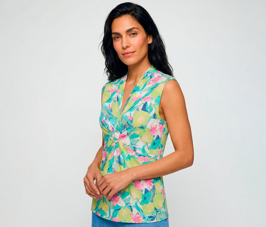 Frau trägt ein ärmelloses Olsen Shirt mit farbenfrohem grünem, pinkem und türkisfarbenem Obst- und Blumenmuster, V-Ausschnitt und dekorativem Ringdetail vorne.