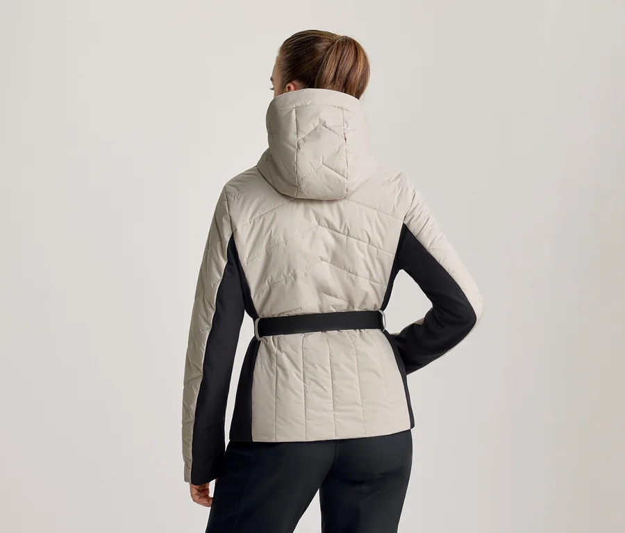 Frau von hinten, trägt eine hellbeige und schwarze Steppjacke mit Kapuze und schwarzem Gürtel, dazu schwarze Hose.