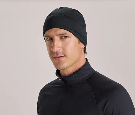 Ein Mann trägt eine schwarze Mütze und ein schwarzes Langarmshirt mit Stehkragen und Reißverschluss und blickt in die Kamera.