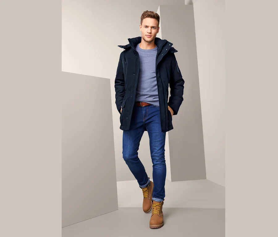 Mann trägt eine Parka, blaue Jeans, einen braunen Gürtel und braune Stiefel.