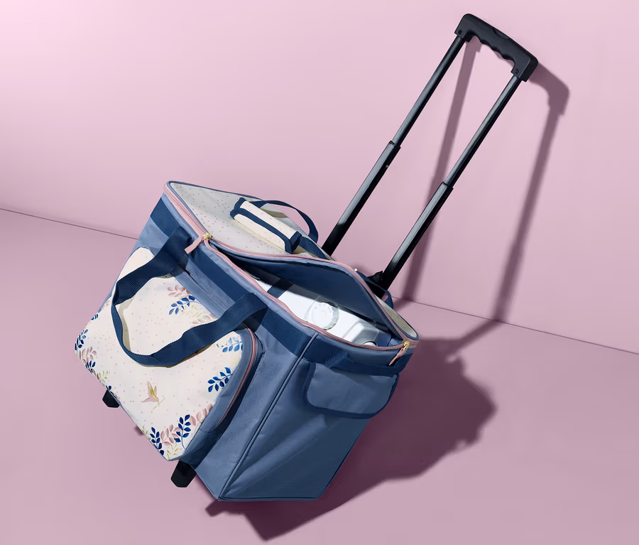 Ein blauer Nähmaschinen-Trolley steht vor einem rosa Hintergrund.