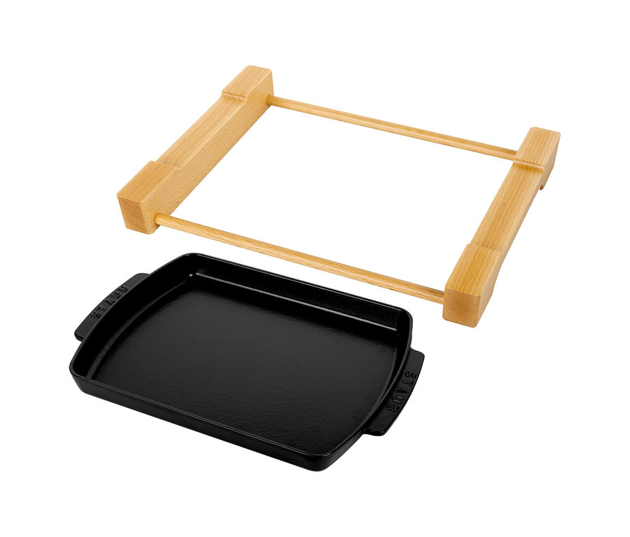 Ein schwarzer STAUB Teller mit Holzunterlage, bestehend aus einer rechteckigen Gusseisenplatte und einem Holzgestell, auf weißem Hintergrund.