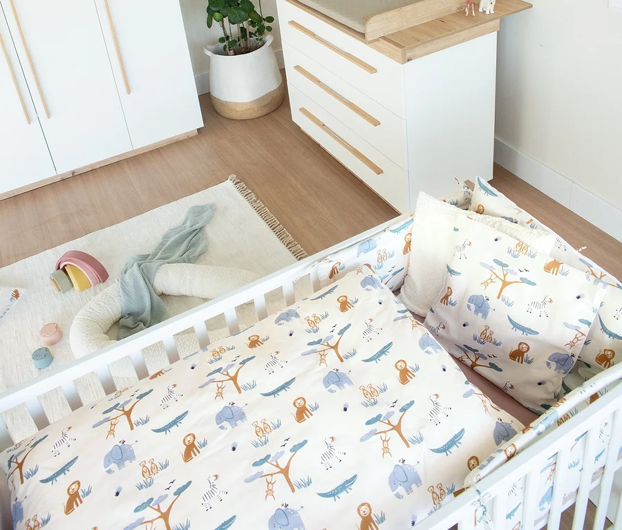 Helles Kinderzimmer mit dem Roba 3-teiligen Kinderzimmer-Set »Lumo«, bestehend aus einem weißen Gitterbett mit Tiermuster-Bettwäsche, einer Wickelkommode und einem Kleiderschrank. Auf dem Boden liegt ein heller Teppich mit Spielzeug.