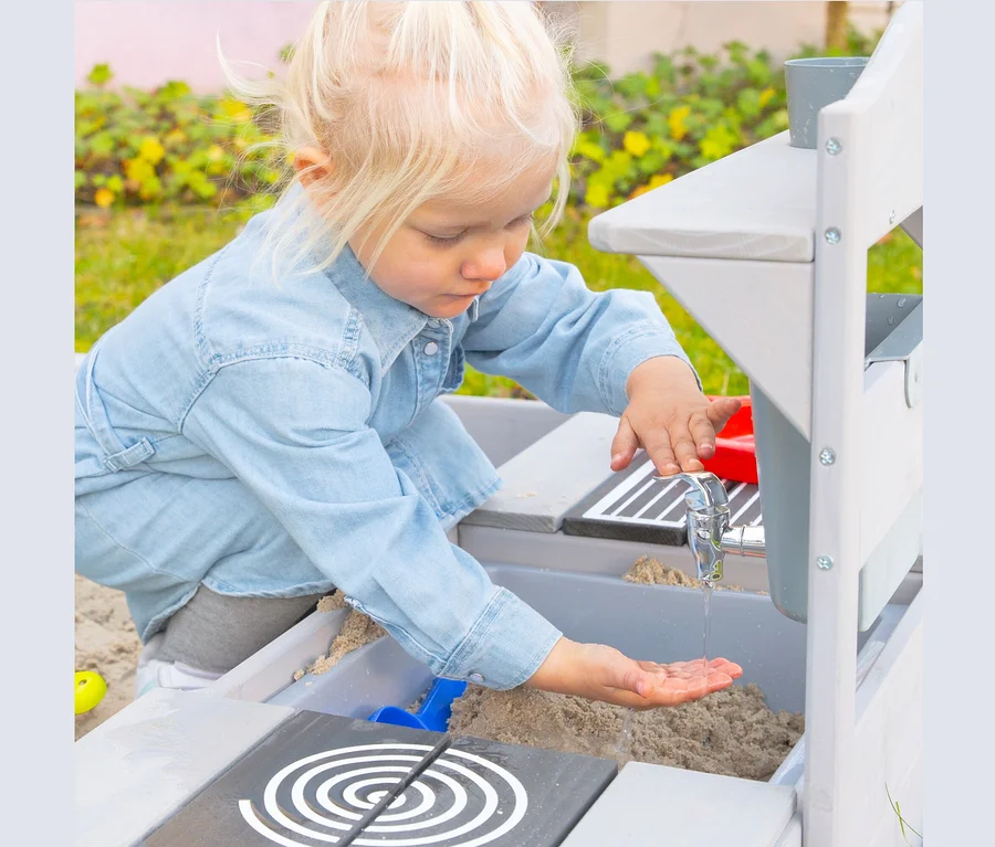 Blondes Mädchen spielt mit Wasser an roba Matschküche zum Hängen.