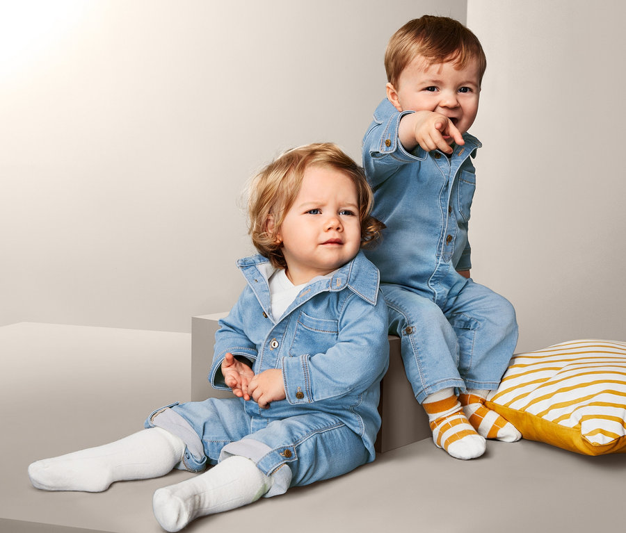 Zwei kleine Kinder posieren vor einem grauen Hintergrund. Beide tragen einen Stretchdenim-Overall.