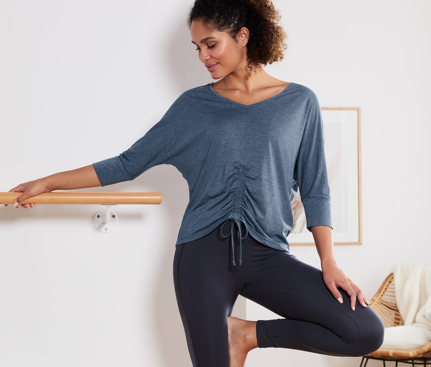 Frau posiert an Ballettstange in blau meliertem 3/4-Sport-und-Yogashirt.