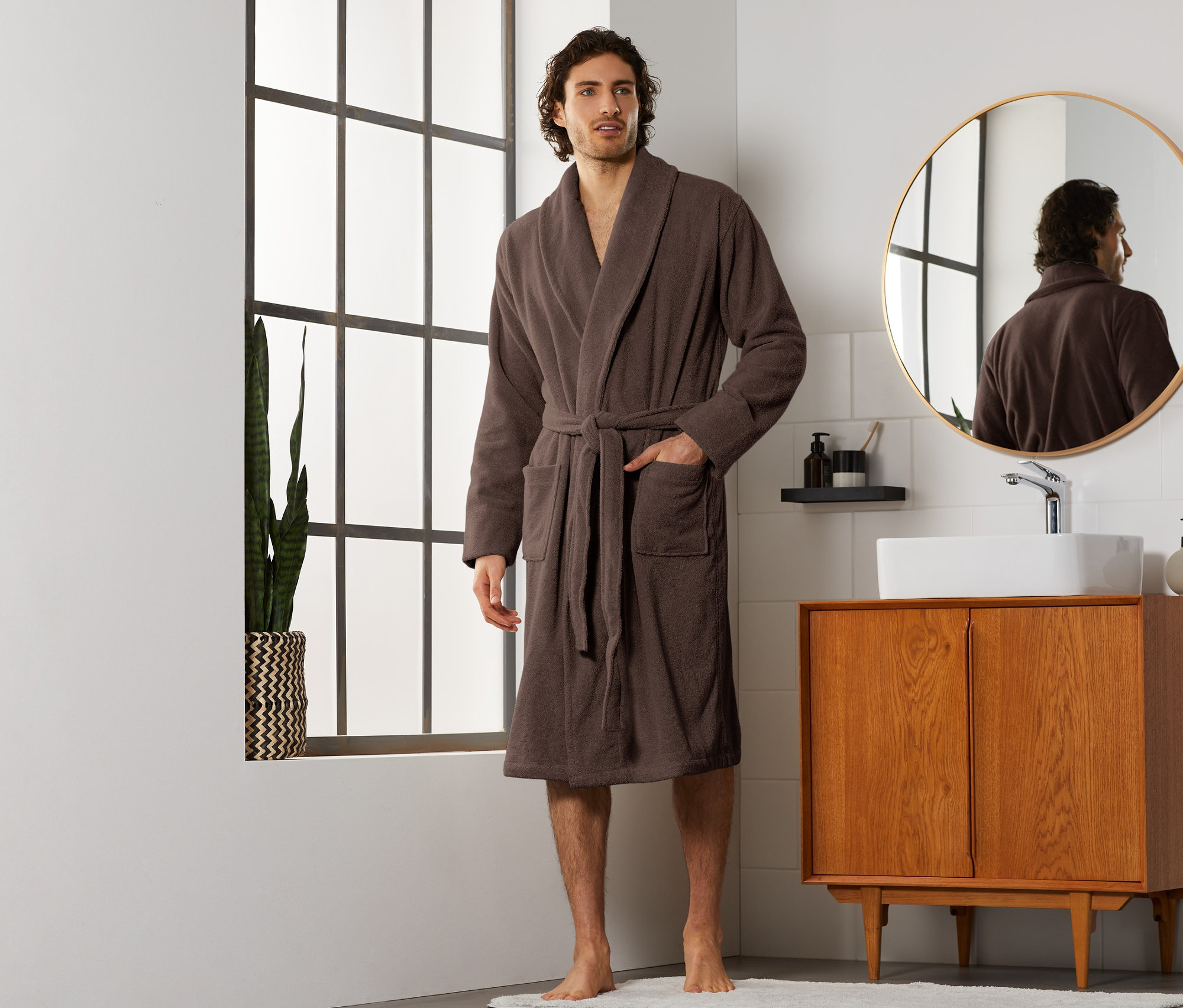 Mann steht im Badezimmer und trägt einen braunen Herren-Bademantel.