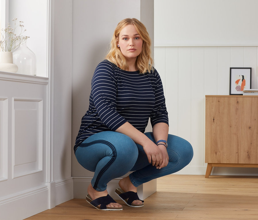 Frau in Jeggings und Shirt mit Fledermausärmeln posiert in Innenräumen.