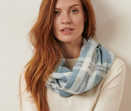 Frau sitzt und trägt einen karierten Fleece-Loop.