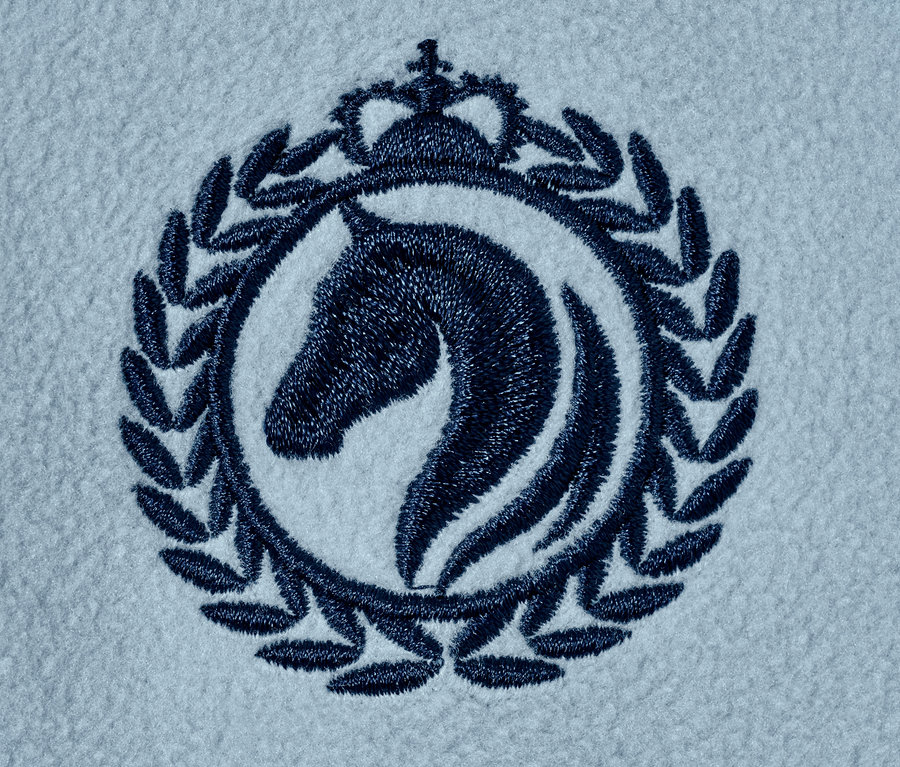 Detail einer blauen Stickerei auf einer hellblauen Fleecejacke aus recyceltem Material, die einen Pferdekopf in einem mit einer Krone und Lorbeerblättern verzierten Kreis darstellt.