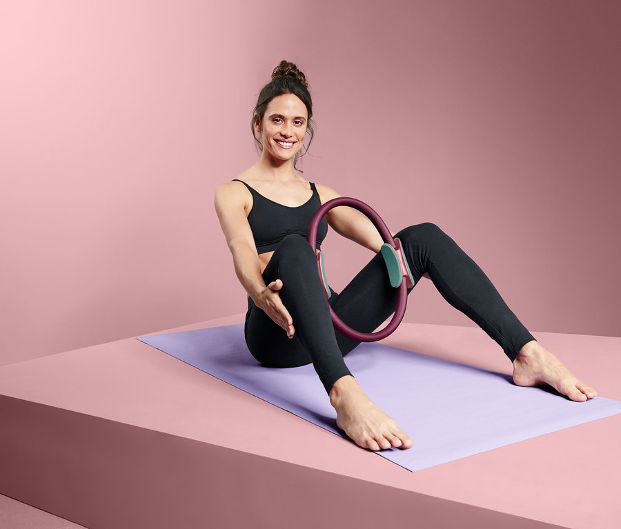 Frau sitzt auf einer Yogamatte und hält einen Pilatesring.
