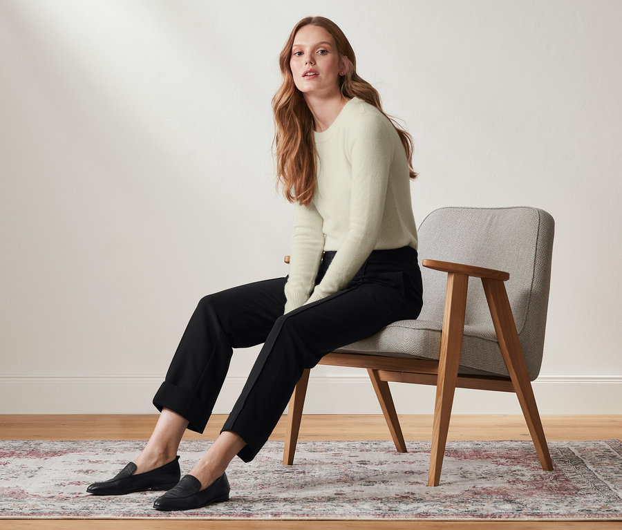Frau sitzt auf einem Stuhl und trägt eine knöchellange Hose.