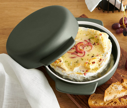 Überbackener Käse im grünen Ofenkäse-Bereiter, mit Trauben, Birne und Brot.