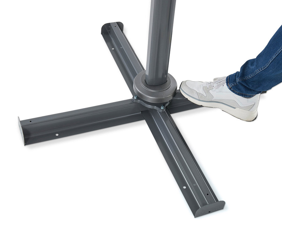 Ein Fuß in einem Turnschuh steht auf dem anthrazitfarbenen Sockel eines Leco Ampelschirms, Ø ca. 330 cm.