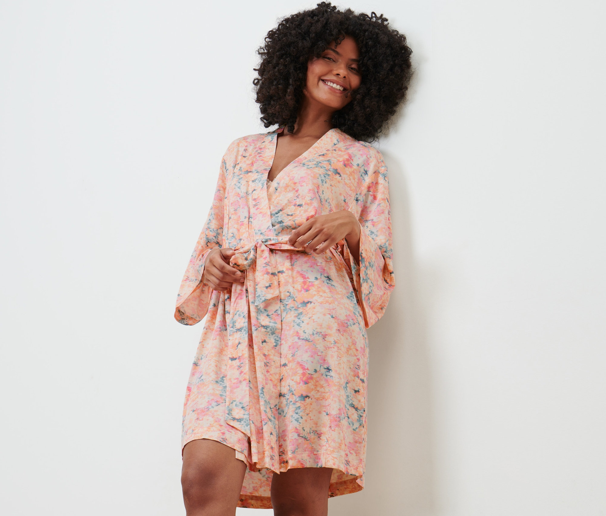 Frau im Morgenmantel steht an einer Wand und lächelt.