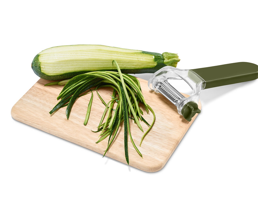 Halbe Zucchini, Zucchinistreifen und 3-in-1-Universalschäler auf einem Schneidebrett.