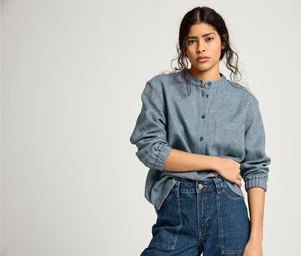 Frau trägt eine blaue NAH/STUDIO Bluse aus Baumwoll-Leinen-Mix und dunkelblaue NAH/STUDIO Mom-Jeans aus recycelter Baumwolle.