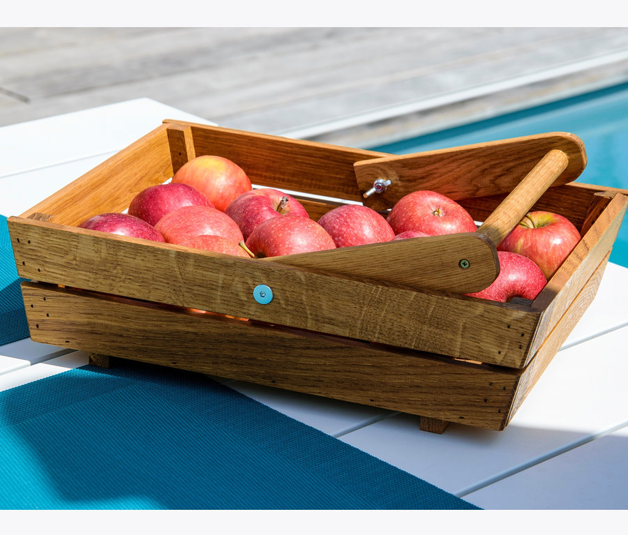 Rote Äpfel in einem hölzernen Erntekorb auf einem weißen Tisch neben einem Pool.