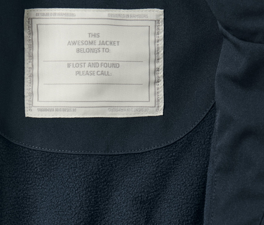 Detailansicht eines Kinder-Regenparkas mit Etikett 'THIS AWESOME JACKET BELONGS TO:'.
