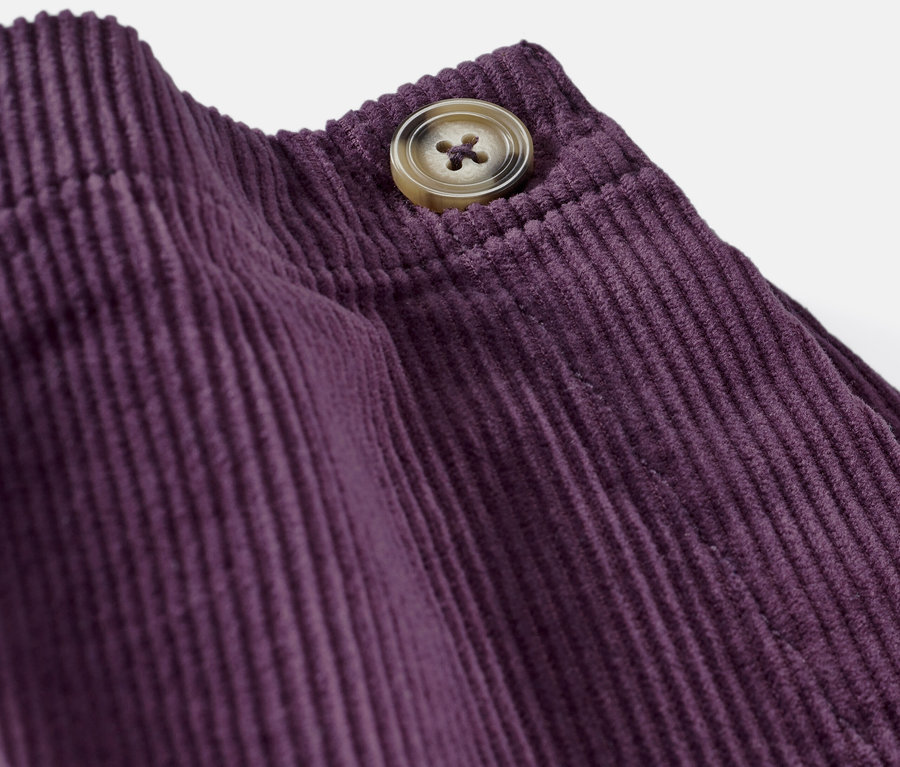 Detailaufnahme eines Kinder-Hosenrocks aus lila Cord mit Knopf.