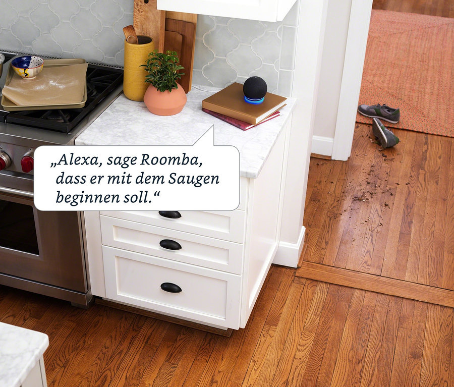Auf einer Küchentheke steht ein Lautsprecher, der sagt: "Alexa, sag Roomba, er soll mit dem Staubsaugen beginnen."
