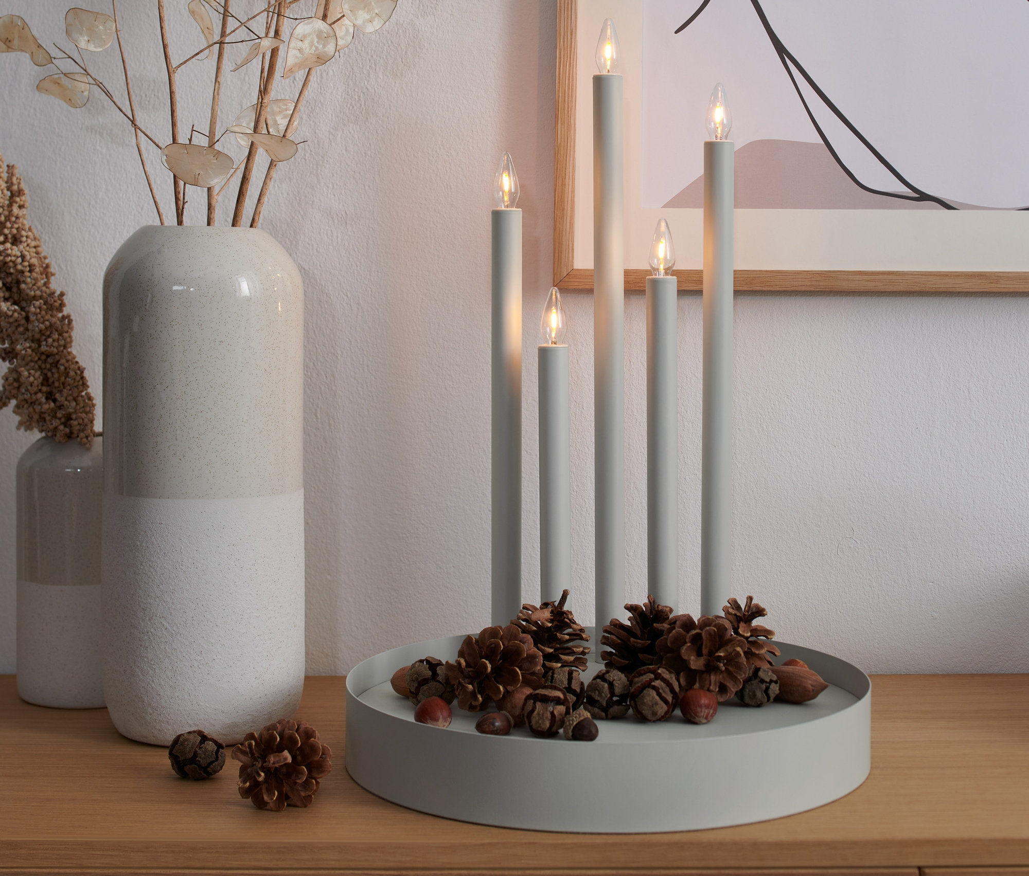Grauer LED-Kerzenleuchter mit fünf Kerzen und Tannenzapfen auf einem Holztisch.