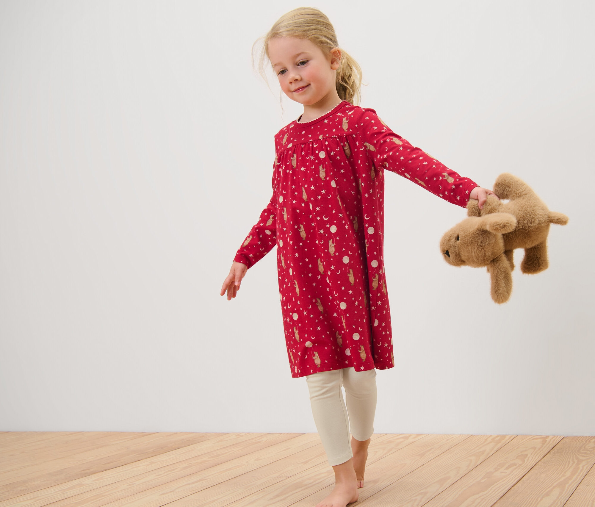 Mädchen im Kinder-Nachthemd mit Leggings hält einen Teddybär.