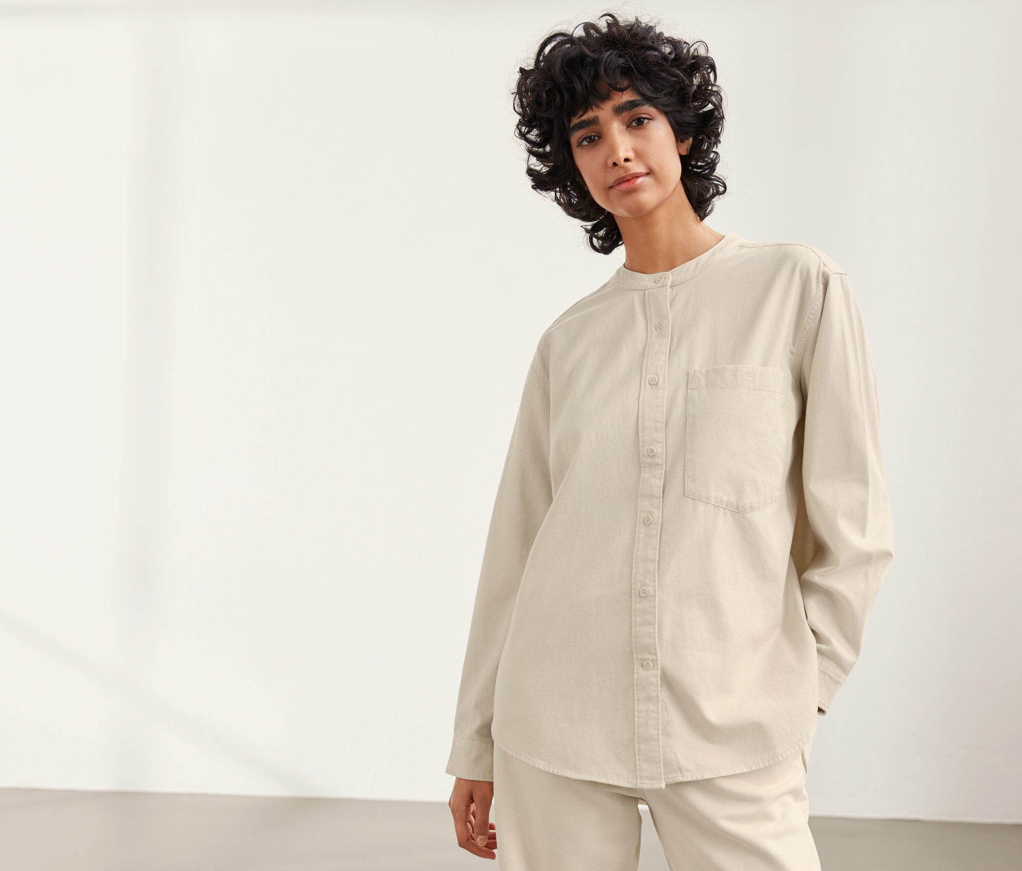 Frau posiert in einem beige-farbenen NAH/STUDIO Hemdbluse aus nachhaltiger Baumwolle.