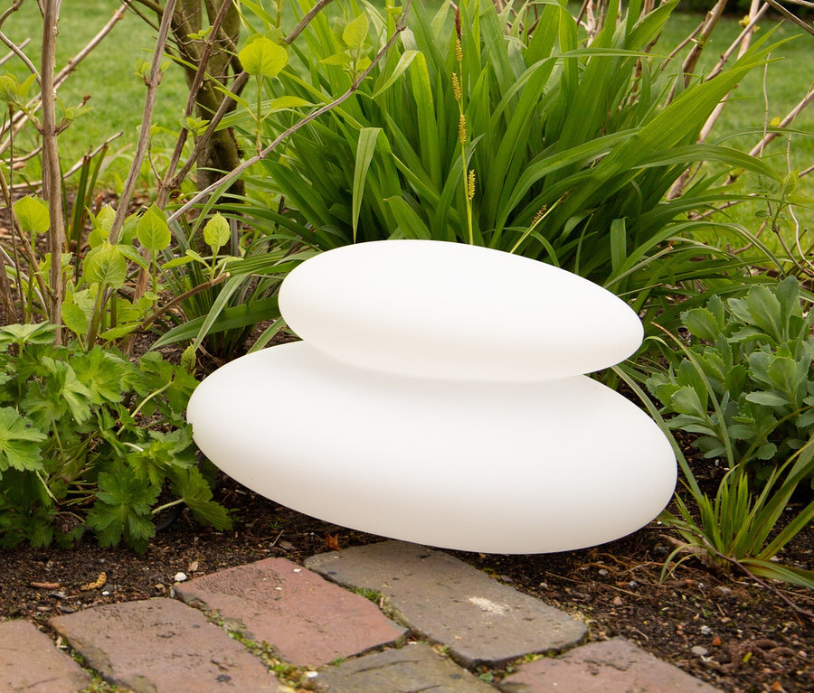 Im Gras zwischen Pflanzen liegt eine weiße 8 seasons design Solar-Leuchte, 39 cm.