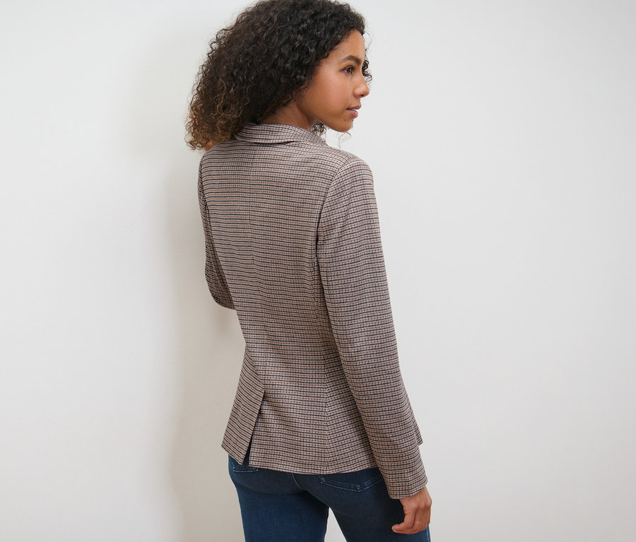 Frau posiert in kariertem Sweatblazer und blauen Jeans.