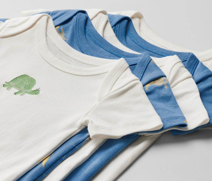 Nahaufnahme von fünf Baby-Kurzarmbodys. Ein weißer Body ist mit einer Schildkröte bedruckt.