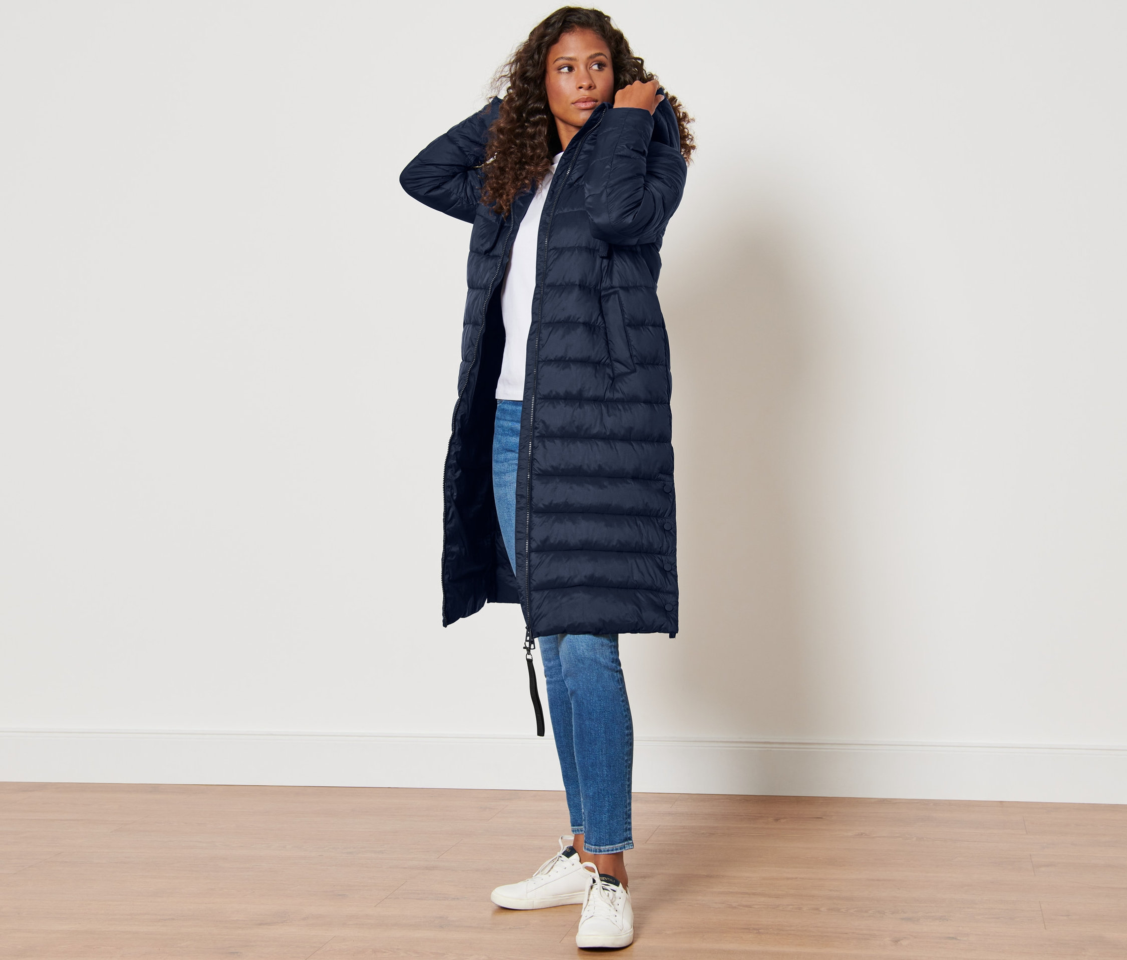 Frau posiert in dunkelblauem Steppmantel mit Kapuze.