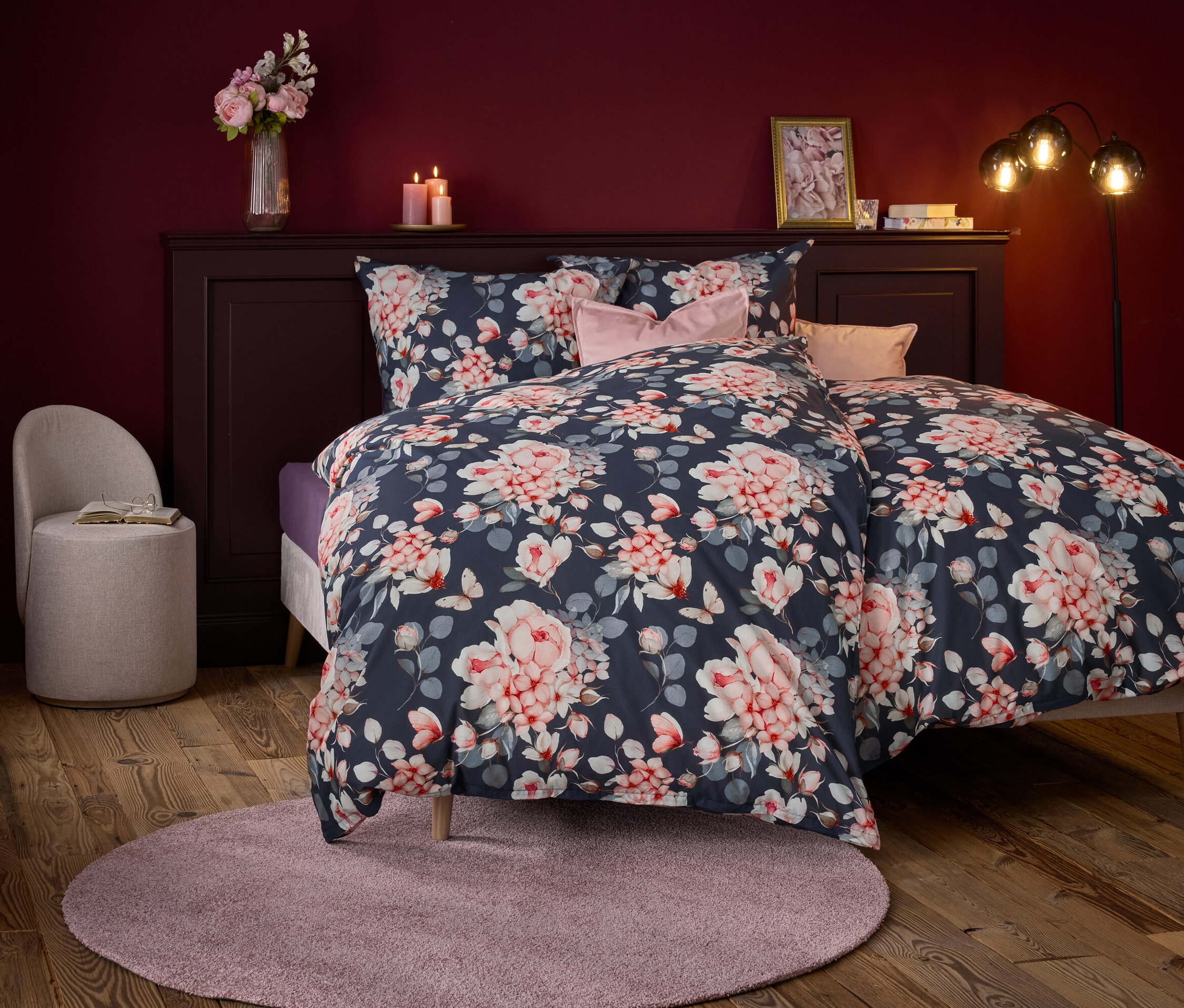 Schlafzimmer mit einem Bett mit floraler Bettwäsche, rosa Kissen und einem runden Teppich.