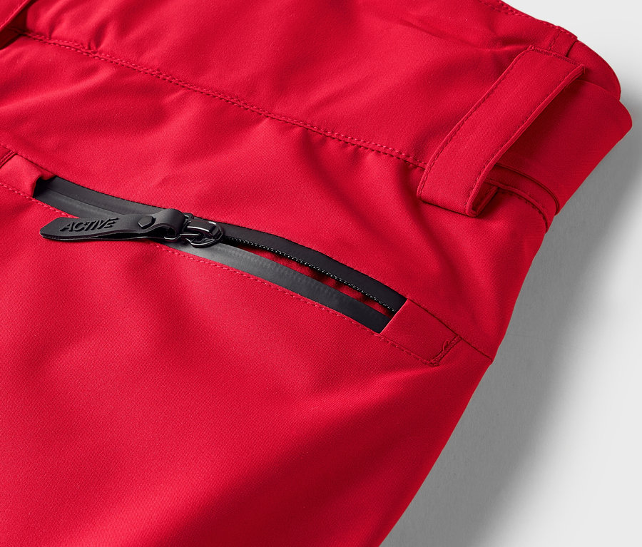 Detail einer roten Hose mit schwarzem Reißverschluss an der Tasche.