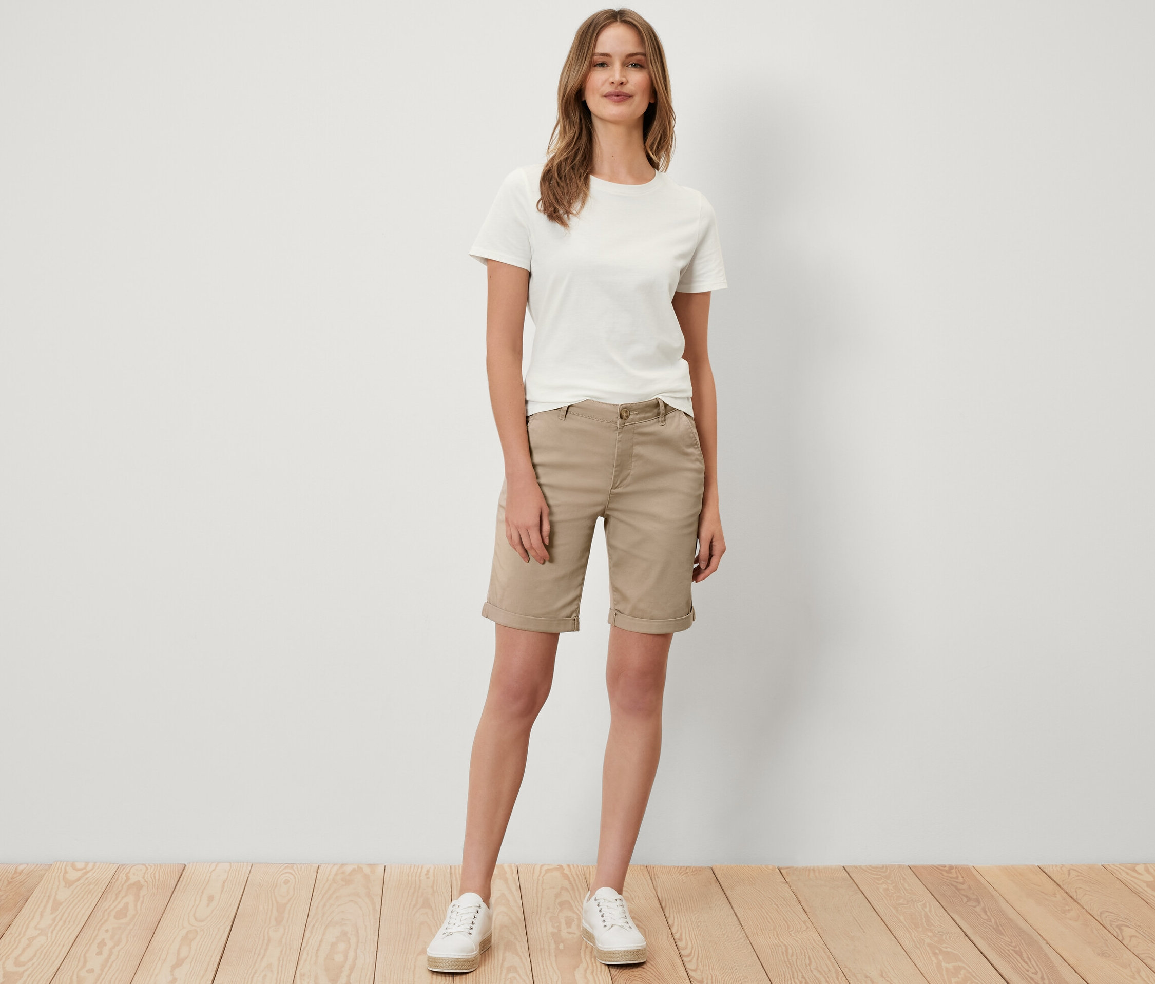 Eine Frau steht und trägt beige Chino-Shorts.