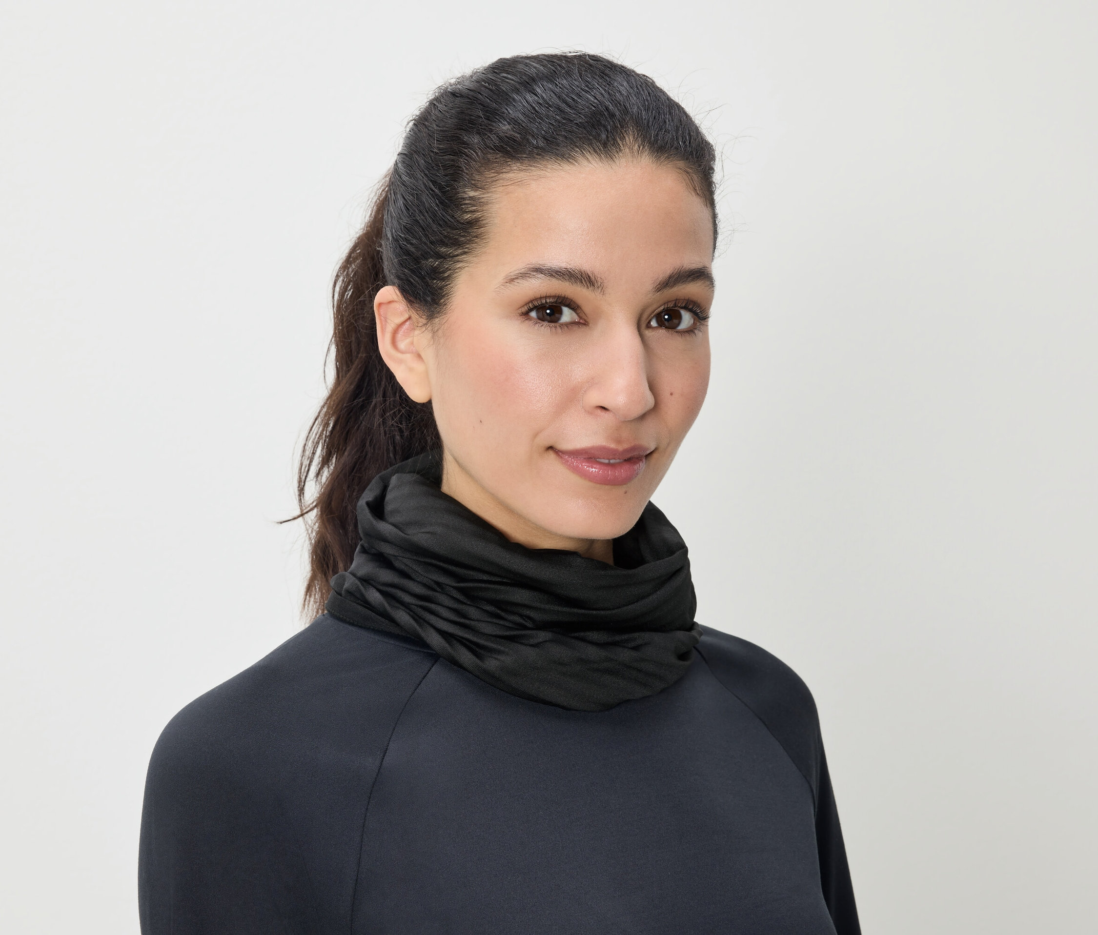 Porträt einer Frau mit braunen, zum Pferdeschwanz gebundenen Haaren, die einen schwarzen Rollkragenpullover trägt.