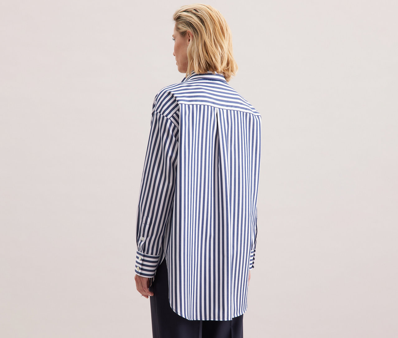 Blonde Frau von hinten, trägt eine gestreifte Seidensticker Oversize Longbluse.