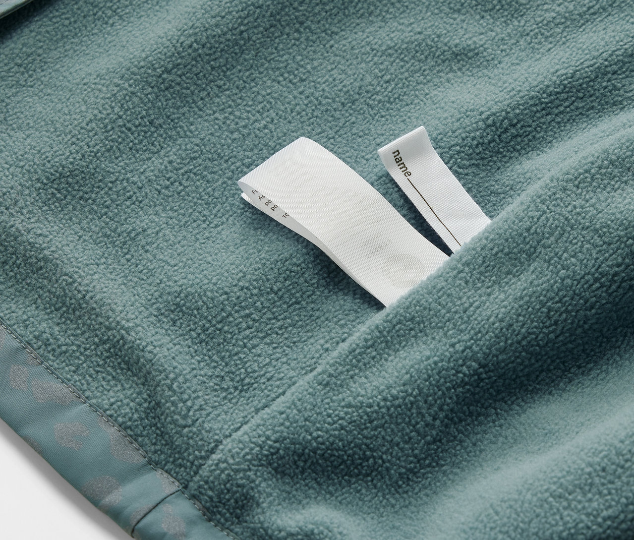 Detailansicht einer Kinder-Thermo-Regenjacke mit reflektierenden Elementen und Namensetikett.