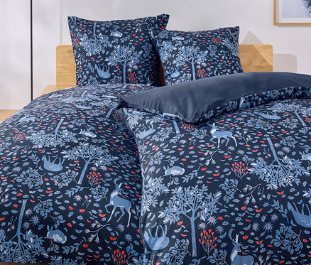 Bett mit blauer Bettwäsche mit Wald-, Baum-, Hirsch- und Kaninchenmuster.
