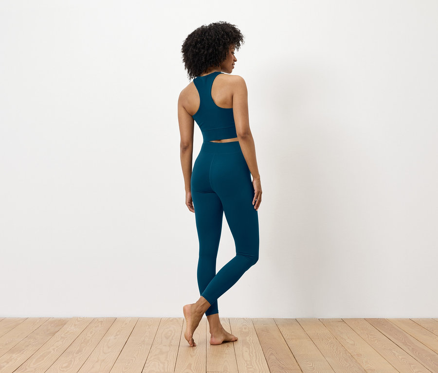 Von hinten ist eine Frau mit dunklen Haaren zu sehen, die einen blauen Sport-BH und Leggings trägt.